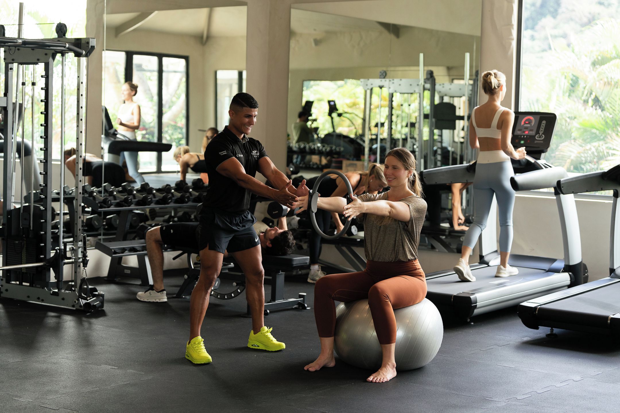 A gym with exercise equipment, a treadmill, and a person using an exercise ball.