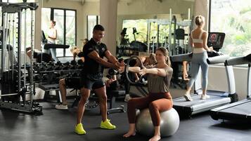 A gym with exercise equipment, a treadmill, and a person using an exercise ball.