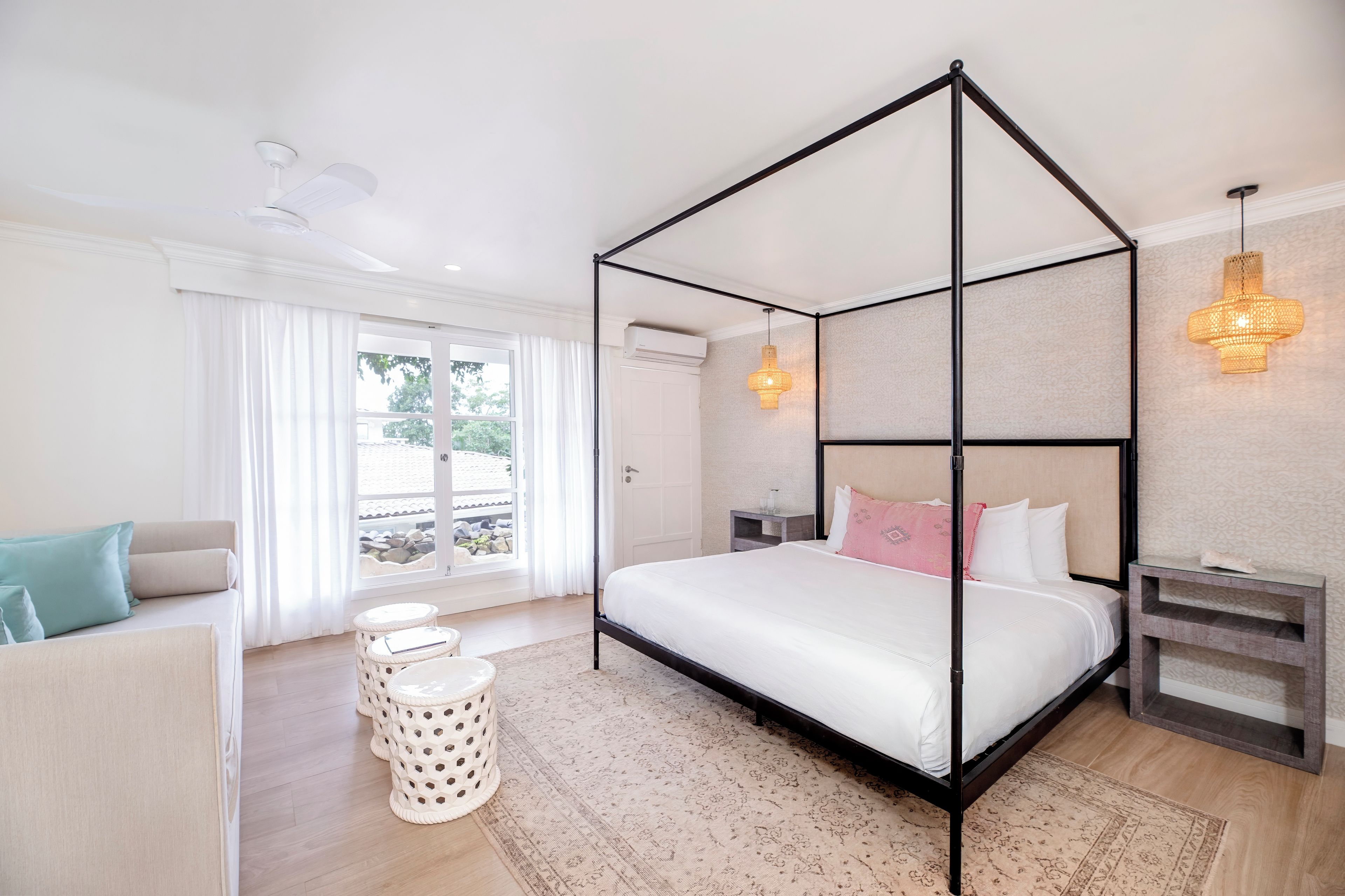 Un dormitorio moderno con una cama con dosel, un sofá, una mesita auxiliar y una ventana con cortinas.
