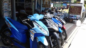 Una fila de motocicletas azules y blancas estacionadas frente a una tienda con un letrero que anuncia precios especiales para alquiler de barcos, autobuses, trenes y aviones.