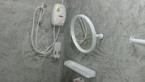 Un baño con pared de mármol, cabezal de ducha de mano, masajeador de mano, botella de champú y dispensador de jabón.