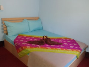 Una cama con colchón azul, cabecera de madera y una manta colorida con estampado de elefantes.