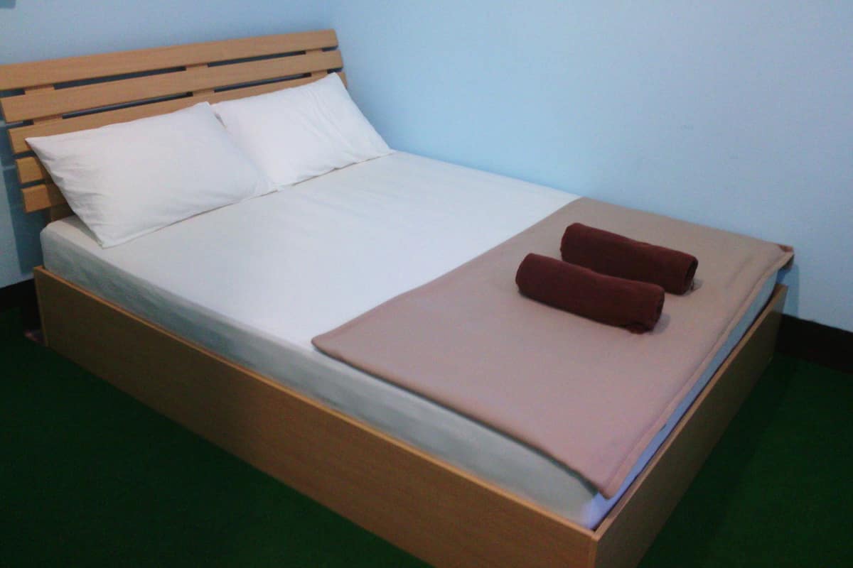 Una cama individual con cabecera de madera, ropa de cama blanca y dos toallas marrones.