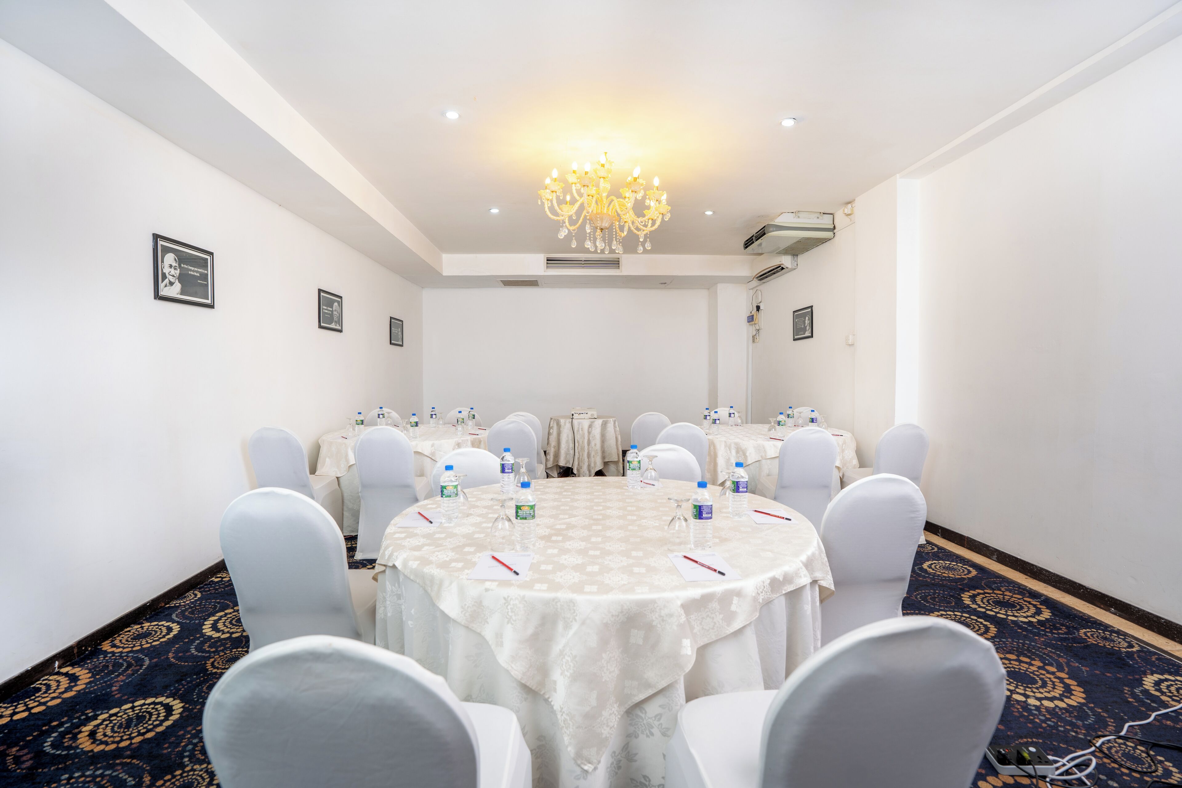 A conference room with round tables, white chairs, and a chandelier.