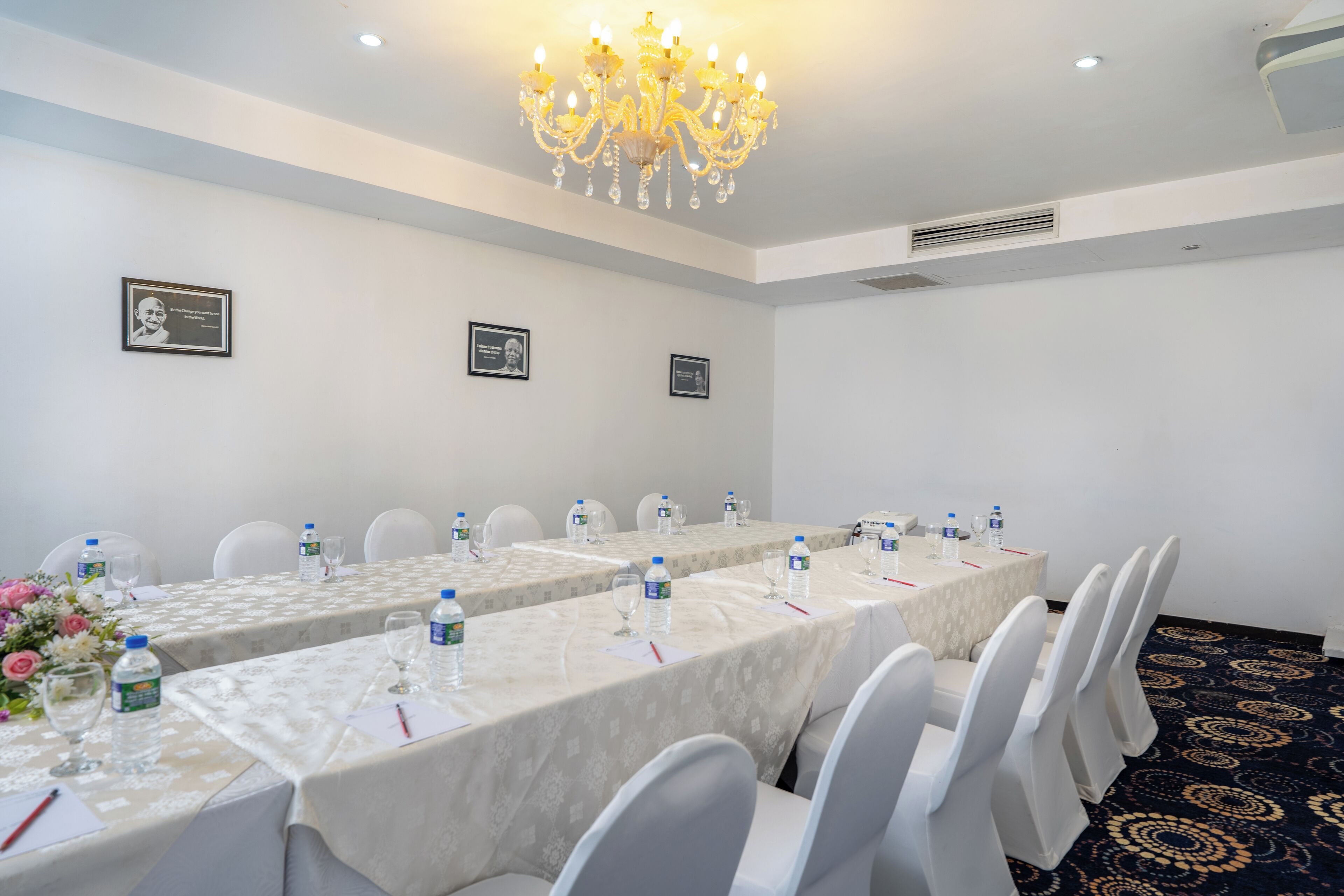 Ein Konferenzraum mit langen Tischen, weißen Stühlen und einer Chandelüster.