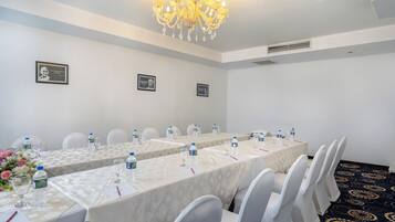 Ein Konferenzraum mit langen Tischen, weißen Stühlen und einer Chandelüster.