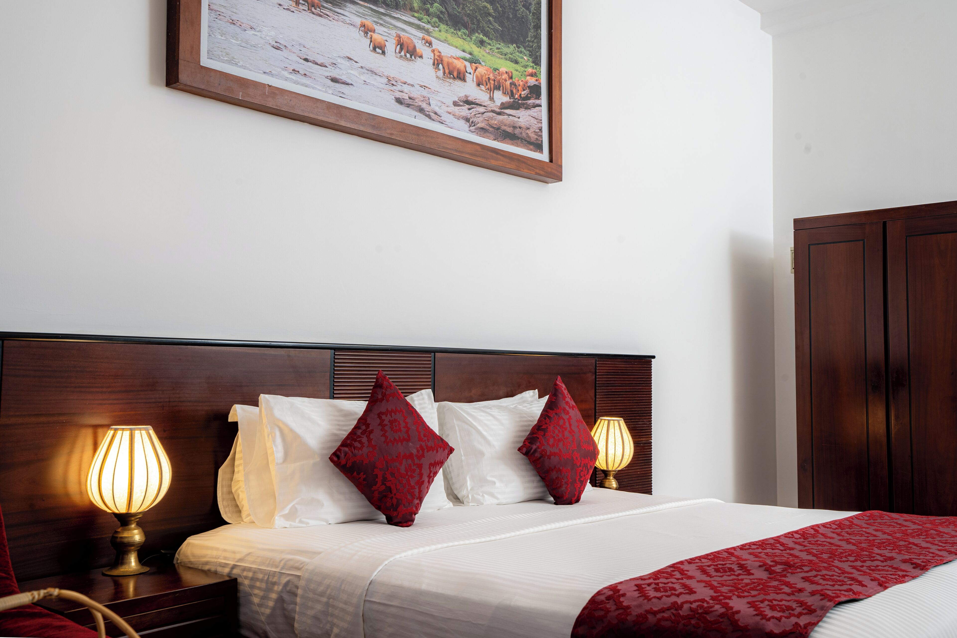 A hotel room with a neatly made bed, two bedside lamps, and a framed picture on the wall.