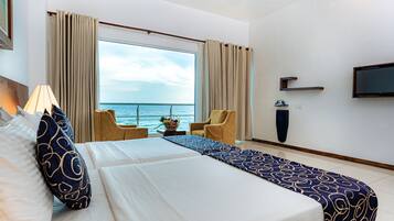 Habitación de hotel con una cama grande, dos sillas, un televisor y vista al mar.