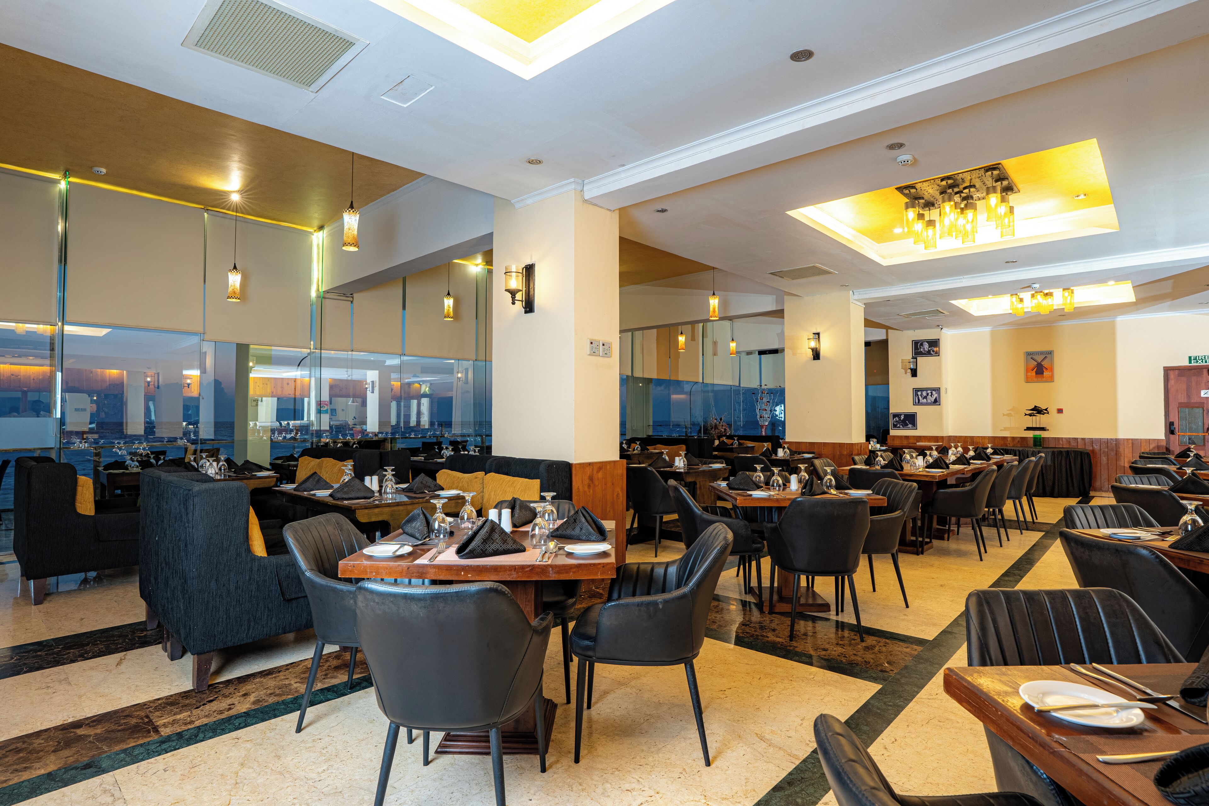 Ein geräumiges Restaurant mit hohen Decken, moderner Beleuchtung und Blick auf die Stadt durch große Fenster.