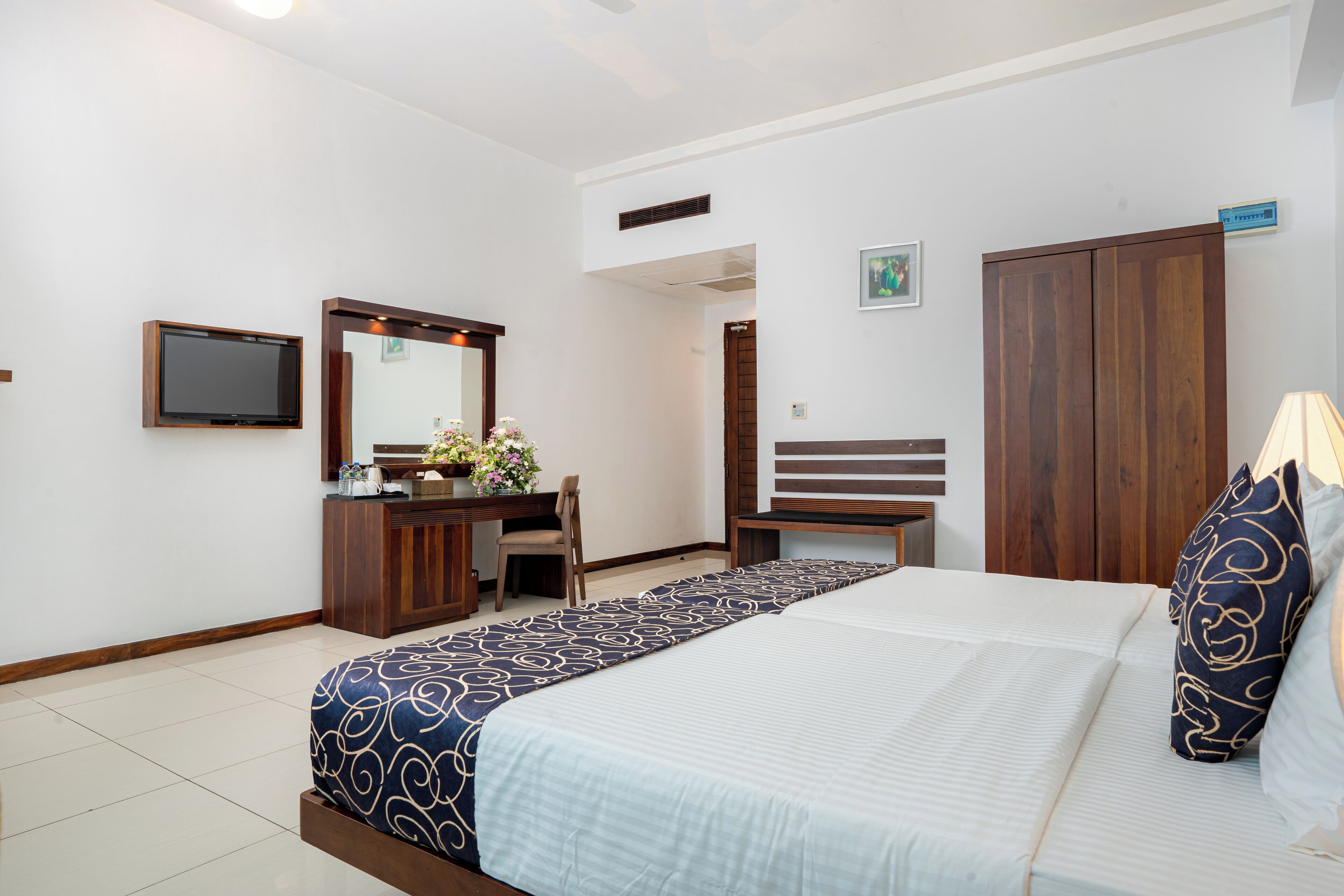A hotel room with a bed, a desk, a chair, a wardrobe, a television, and a mirror.
