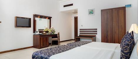 A hotel room with a bed, a desk, a chair, a wardrobe, a television, and a mirror.