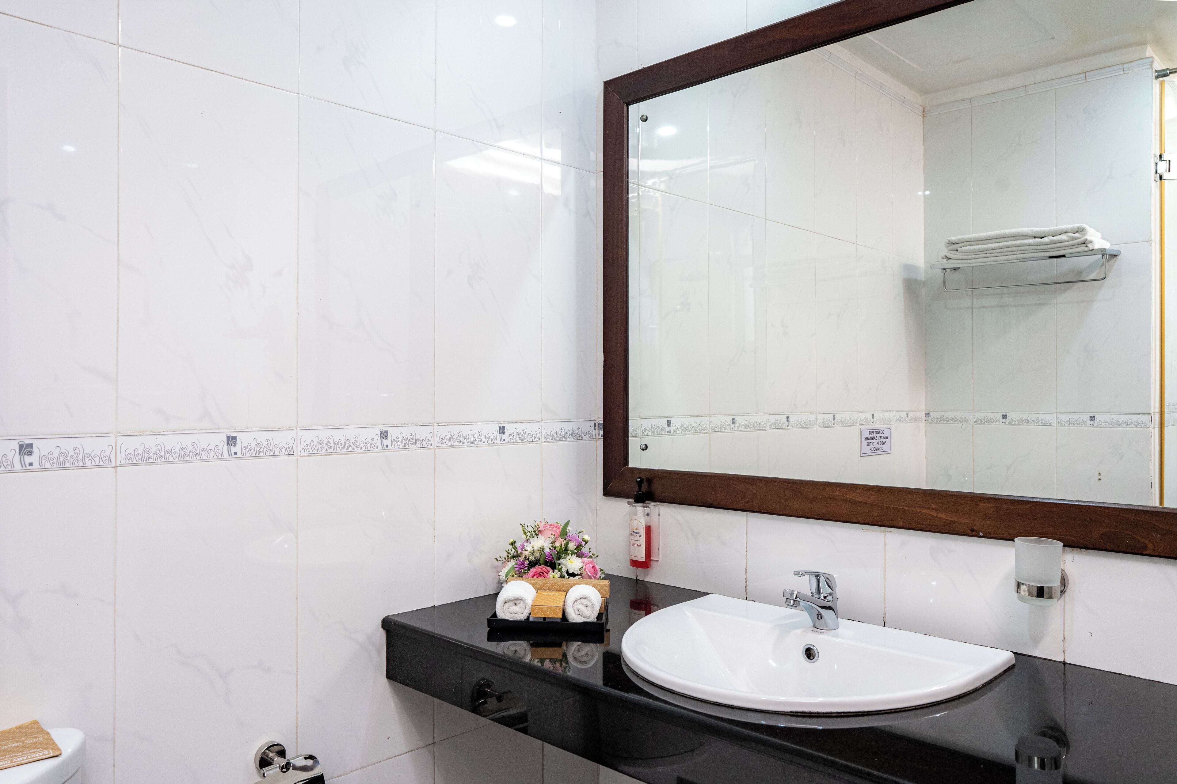 Casa de banho com lavatório branco, bancada preta e um espelho grande.