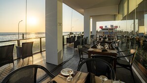 Un restaurante con vista al océano, mesas con sillas y barandilla de cristal.