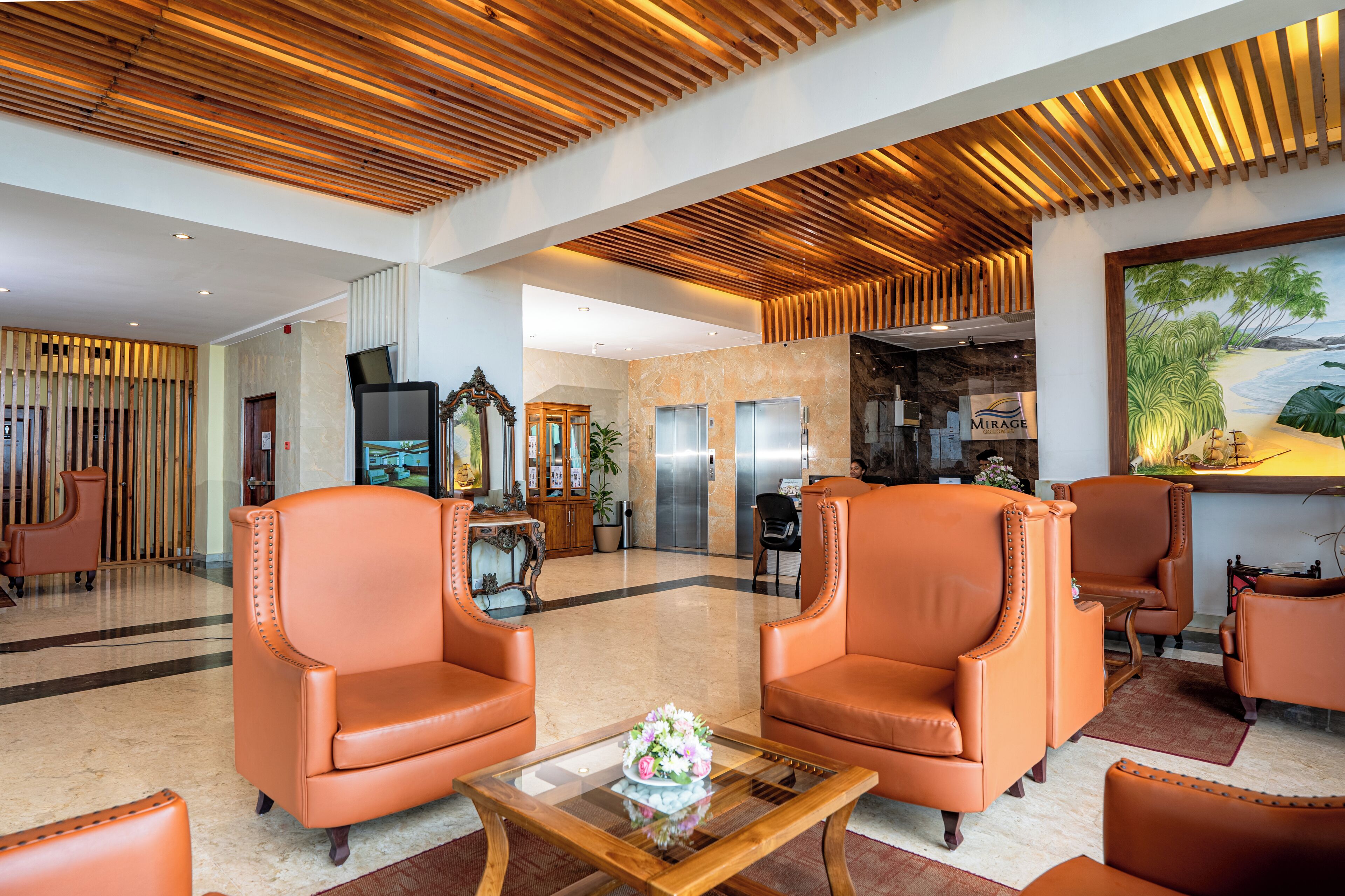 Eine Lobby mit Ledersesseln, einem Glastisch, einer Rezeption und einem Gemälde mit Strandmotiv.
