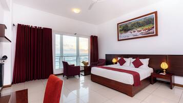 A hotel room with a large bed, two chairs, a nightstand, a lamp, and a painting of a landscape.