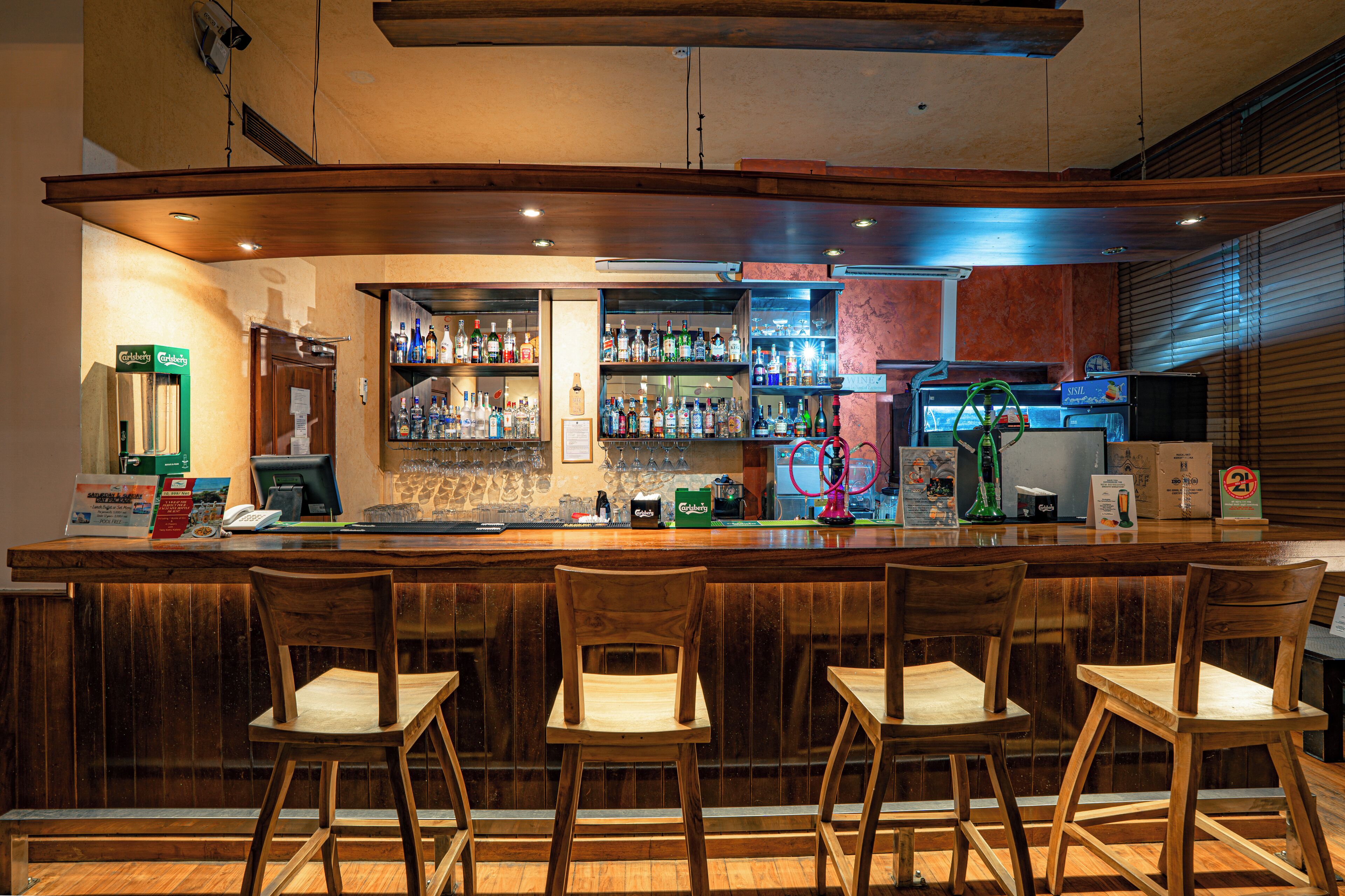 A bar with wooden chairs, a counter with various bottles, and a cash register.