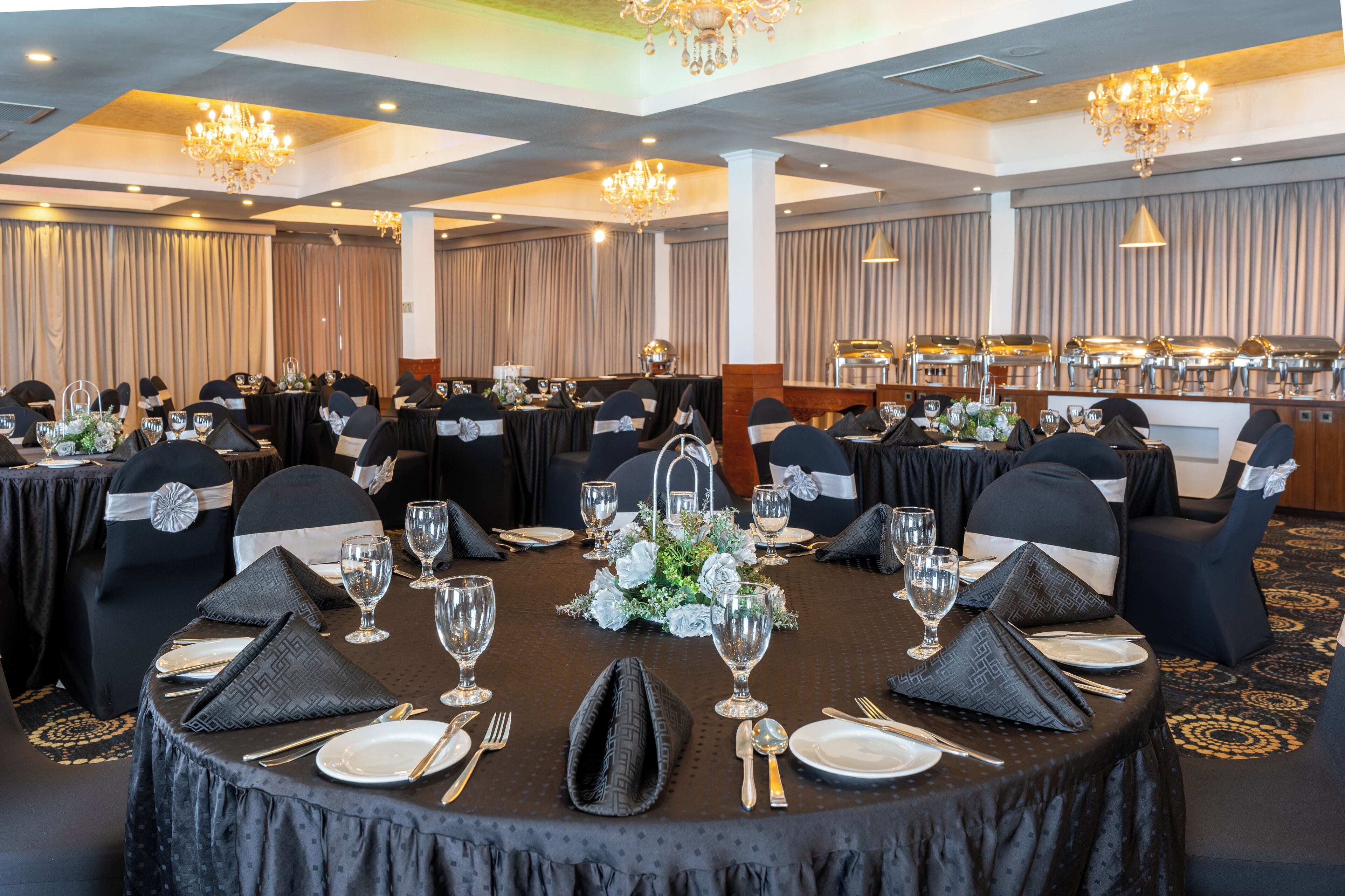 Une salle de banquet avec des tables rondes dressées pour un événement formel, avec des nappes noires, des serviettes blanches et des couverts en argent.