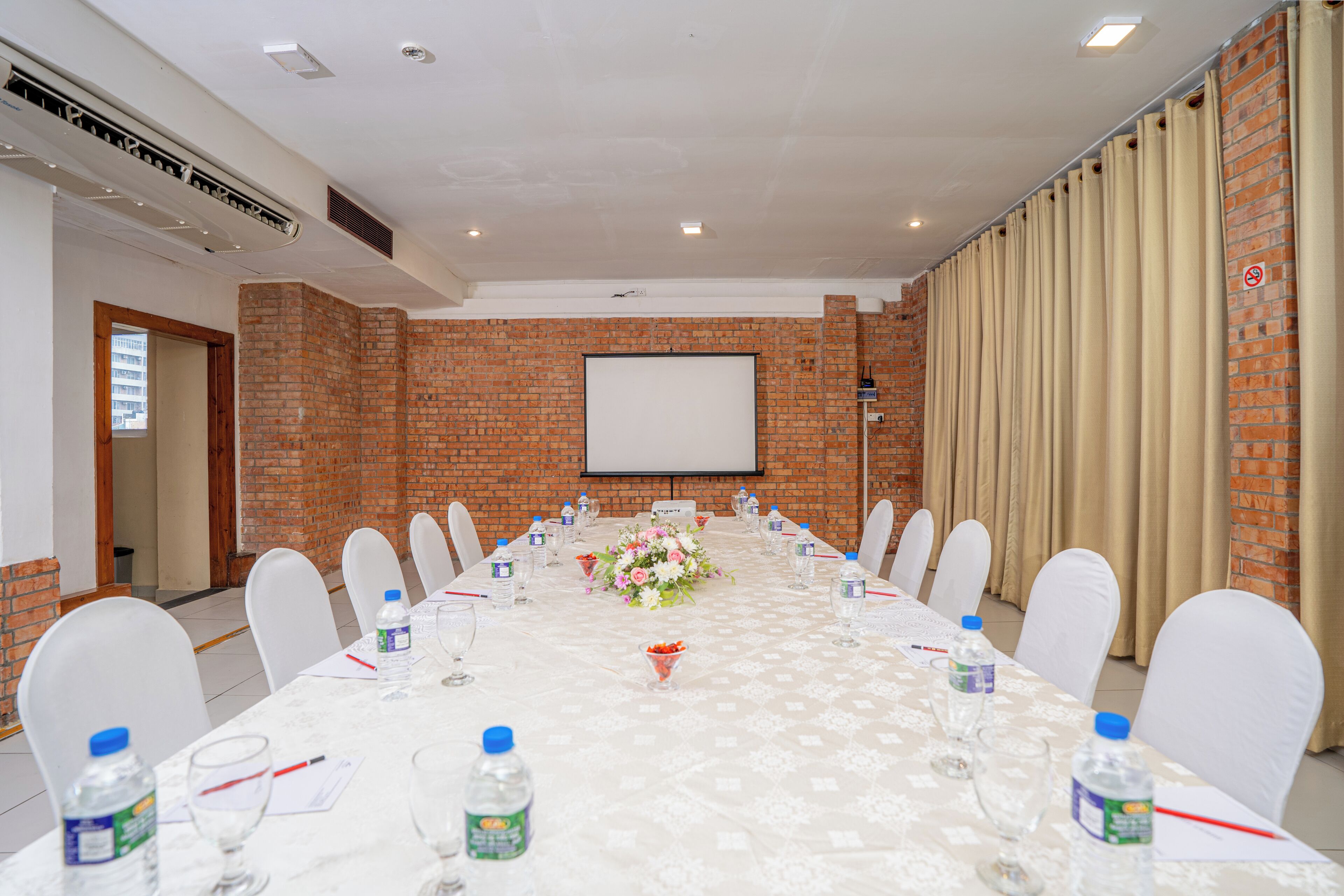 A conference room with a long table, white chairs, water bottles, and a projector screen.