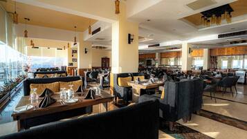 Un restaurante espacioso con techos altos, amplias ventanas y diferentes opciones de asientos, como cabinas y mesas.