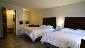 Quarto de hotel com duas camas, banheiro e pequena área de trabalho.