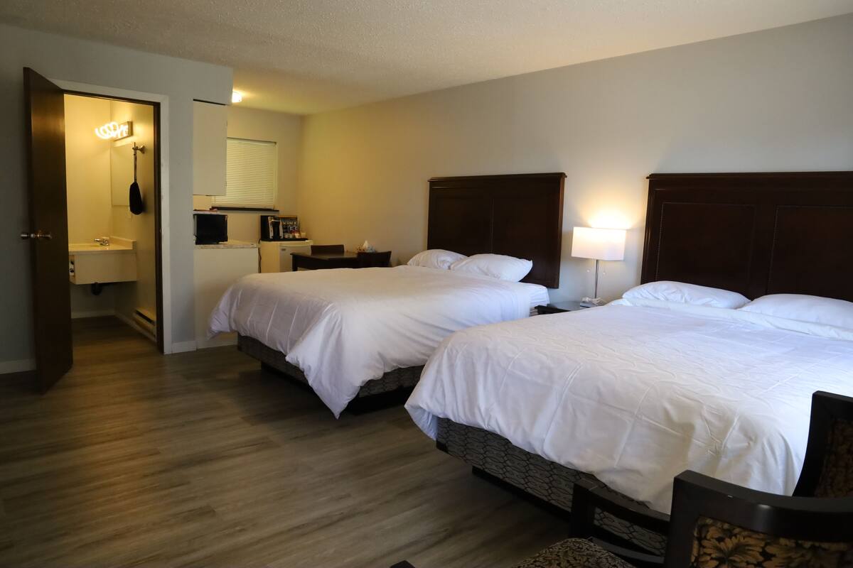 Habitación de hotel con dos camas, baño y una pequeña zona de escritorio.