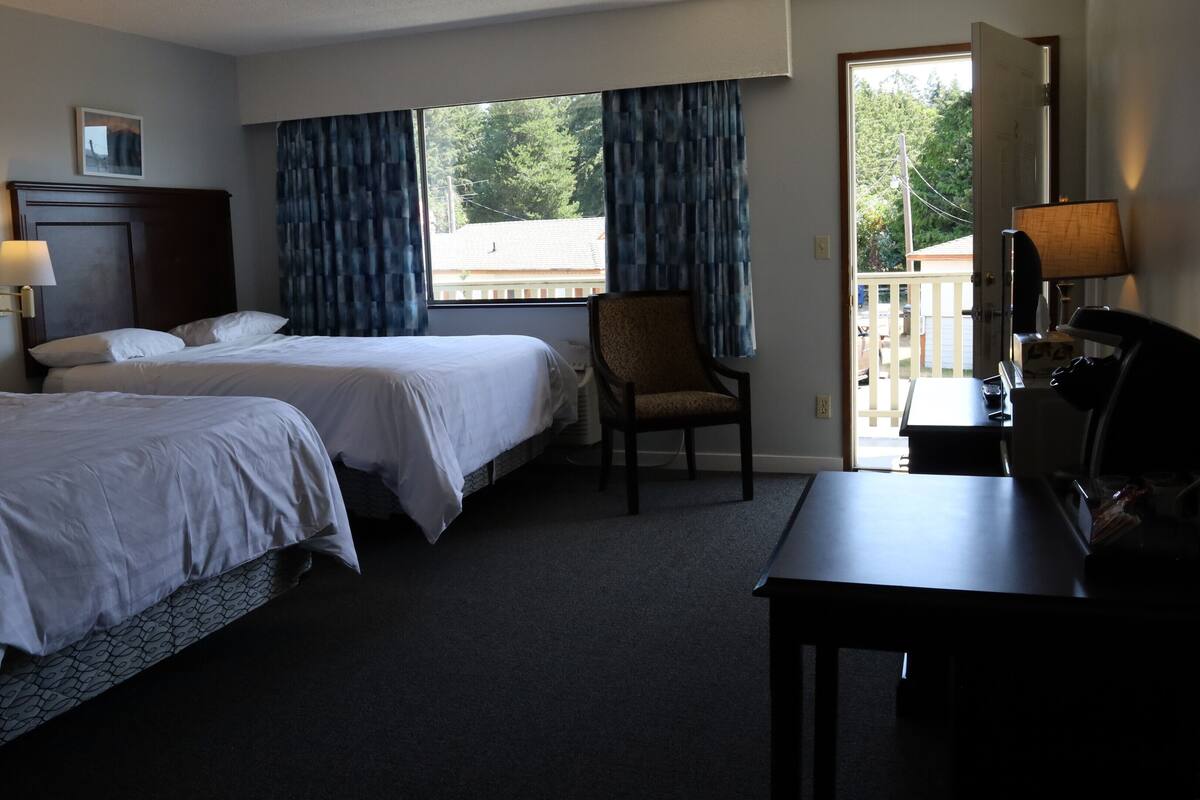 Una habitación de hotel con dos camas, un escritorio, una silla y vistas al exterior.