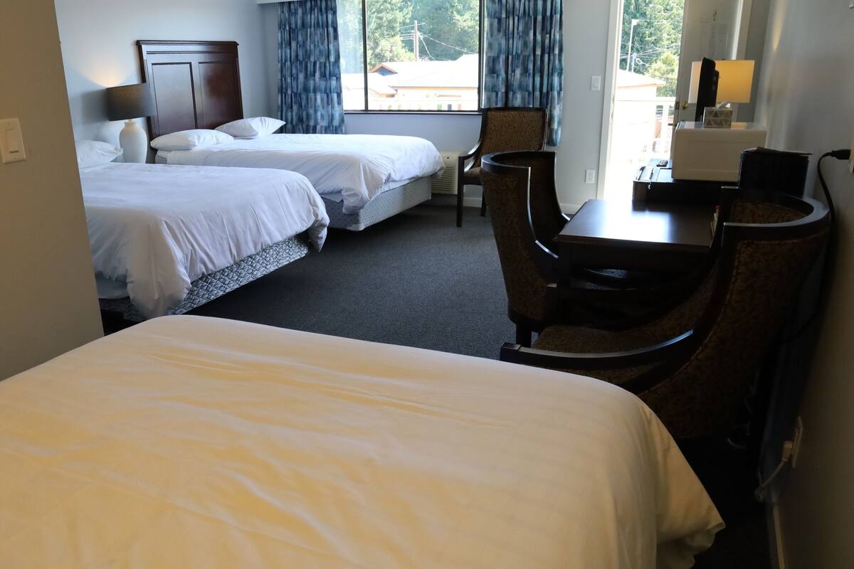 Una habitación de hotel con dos camas individuales, un escritorio con una silla y un ventanal con cortinas.