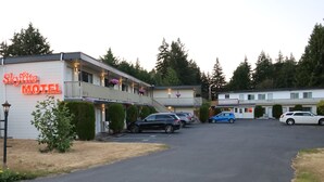 Um motel com um letreiro de neon, várias vagas de estacionamento e uma entrada com acesso por um caminho.