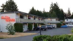 A motel with a neon sign, multiple parking spaces, and a covered walkway. - Skylite Motel (Parksville)
