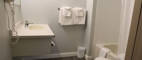 Casa de banho com lavatório, sanita, chuveiro e secador de cabelo preso à parede.