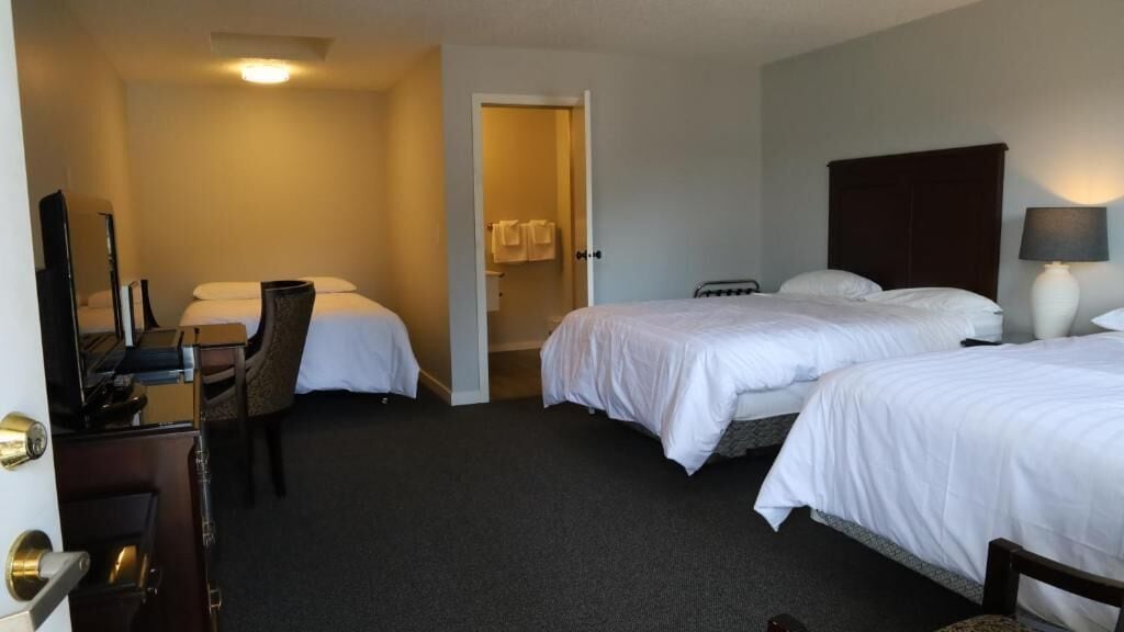 Una habitación de hotel con dos camas, un escritorio, una silla, un televisor y una lámpara.