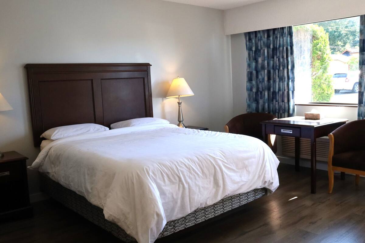 Una habitación de hotel con una cama grande, dos lámparas de noche, un escritorio con una silla y una ventana con cortinas.