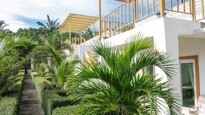 A modern building with a white exterior, a balcony with wooden railings, and lush greenery including palm trees. - KeereeLay (Ko Lanta)