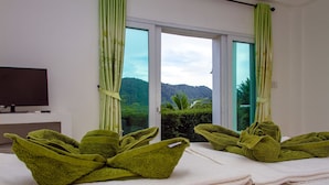 A room with two green towels arranged on a bed, a television on the wall, and a view of a mountain through the window. - KeereeLay (Ko Lanta)