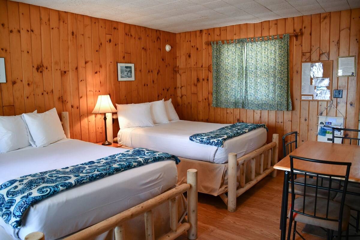 Une chambre avec deux lits, une table en bois et une fenêtre avec un rideau.