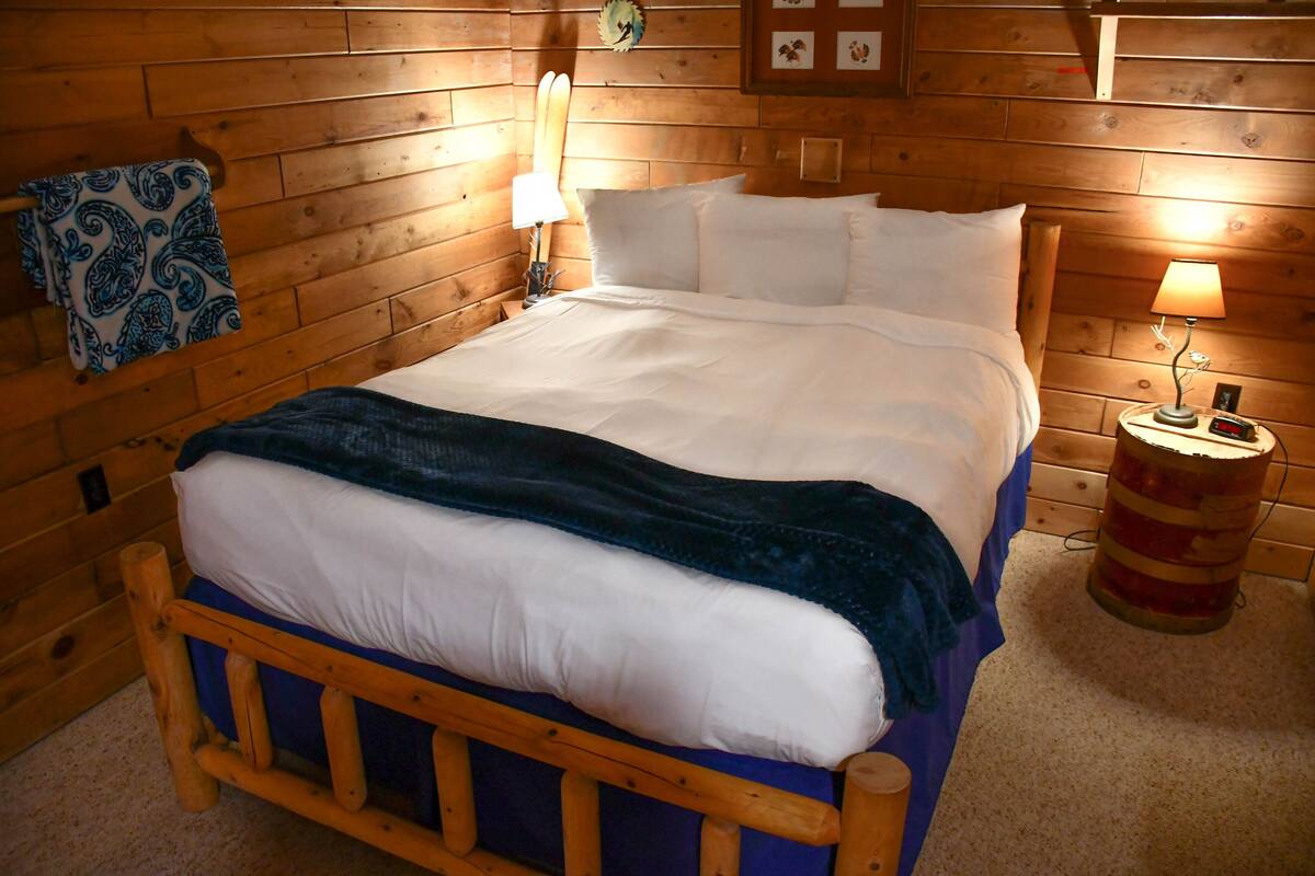 Un lit en bois avec une literie blanche, une couverture bleue et deux lampes de chevet.
