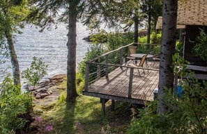 A wooden deck with a railing overlooking a body of water, surrounded by trees and greenery.