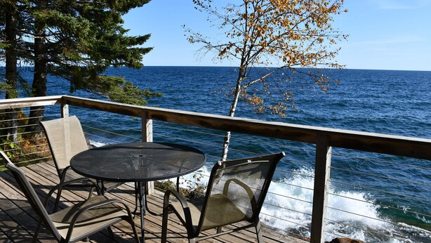 Une terrasse en bois avec une table ronde et deux chaises, donnant sur une étendue d’eau.