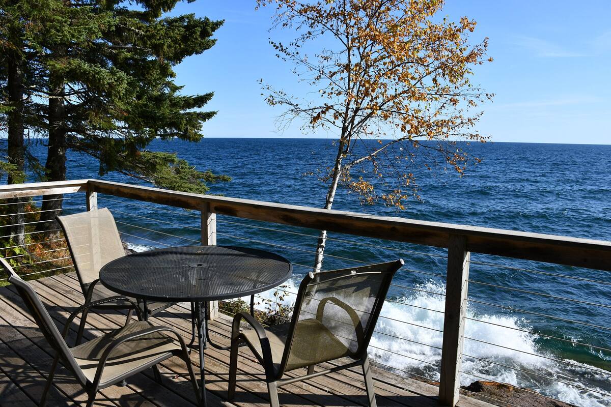 Une terrasse en bois avec une table ronde et deux chaises, donnant sur une étendue d’eau.