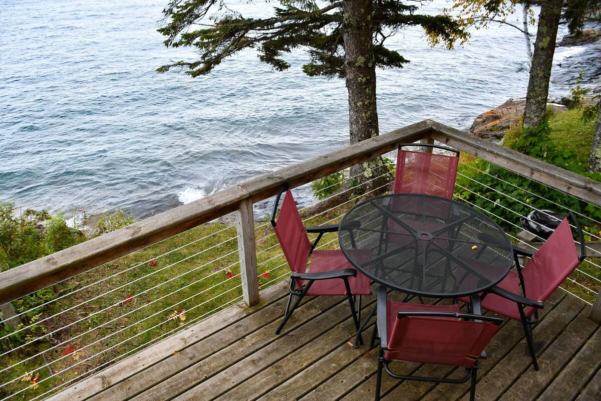 Une terrasse en bois avec une table ronde et quatre chaises, donnant sur une étendue d’eau.