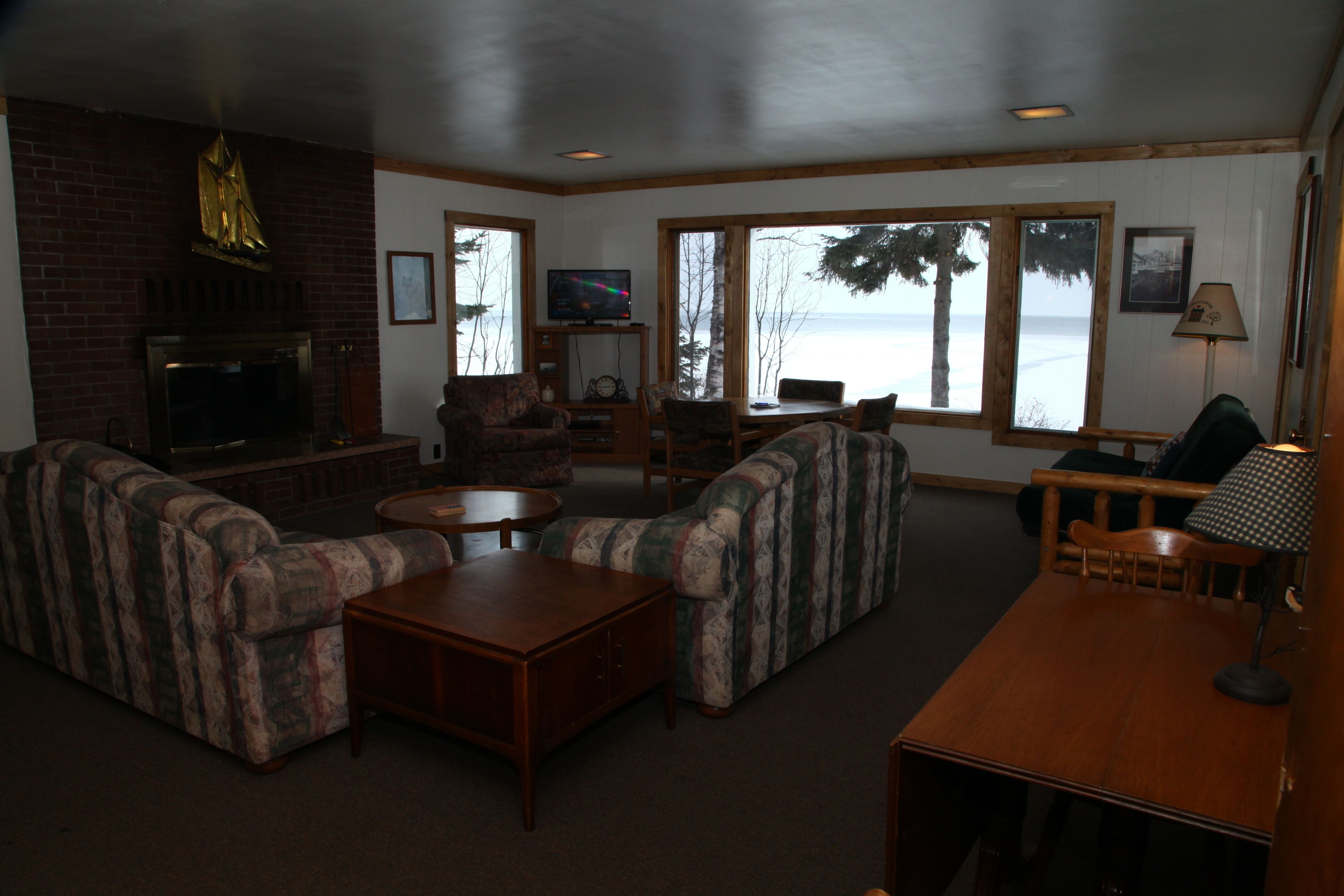 A cozy living room with a fireplace, comfortable seating, a television, and large windows overlooking a body of water.