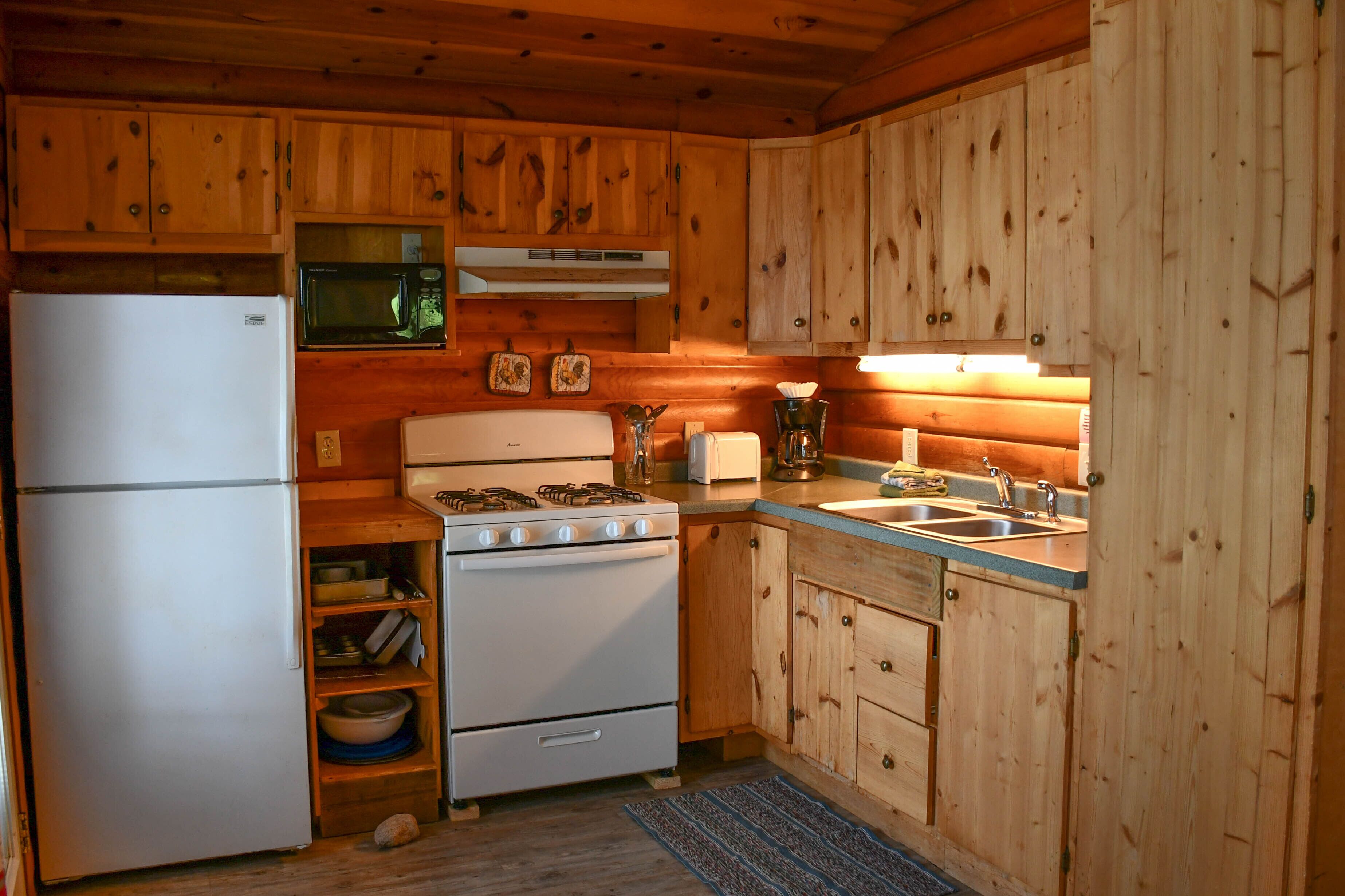 A compact kitchen with wooden cabinets, a white refrigerator, a microwave, a stove, and a sink.