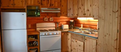 A compact kitchen with wooden cabinets, a white refrigerator, a microwave, a stove, and a sink.