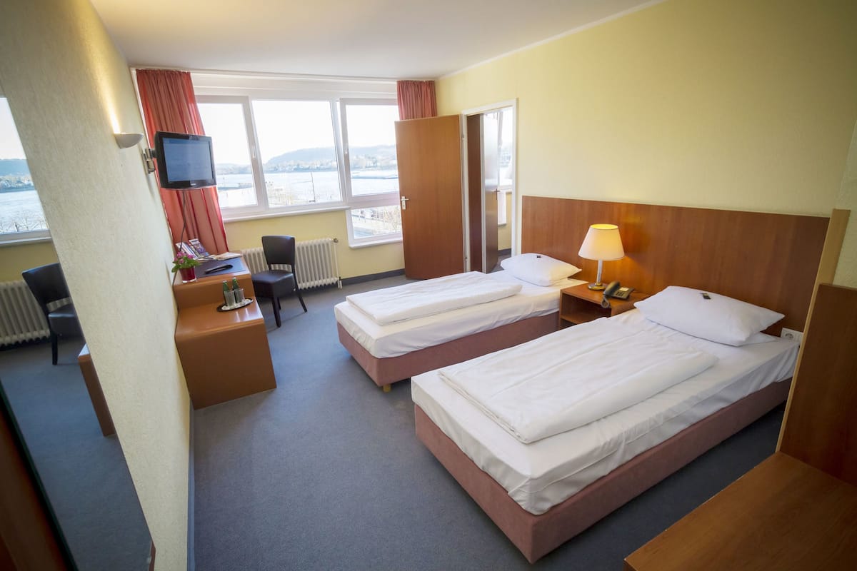 Habitación de hotel con dos camas, un escritorio con computadora, una silla y televisor.