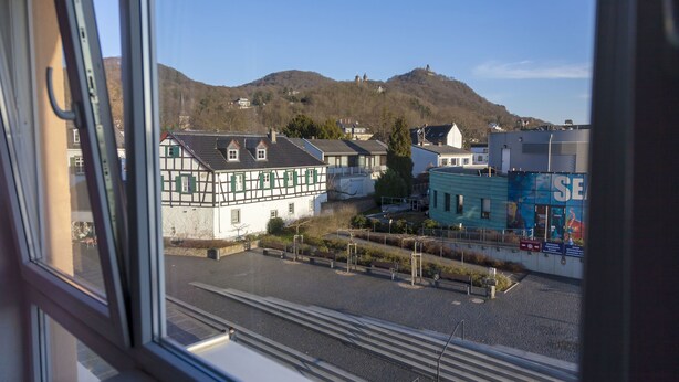 Vista desde una ventana de un edificio que muestra un estacionamiento, una pequeña colina con casas y un gran edificio azul con señalización.