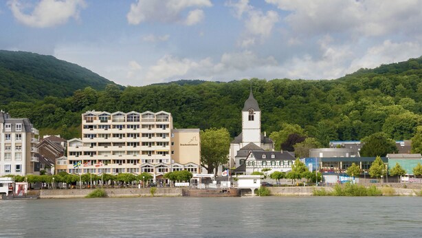 Eine Stadt am Flussufer mit einem Hotel, einer Kirche und einem Berg im Hintergrund.