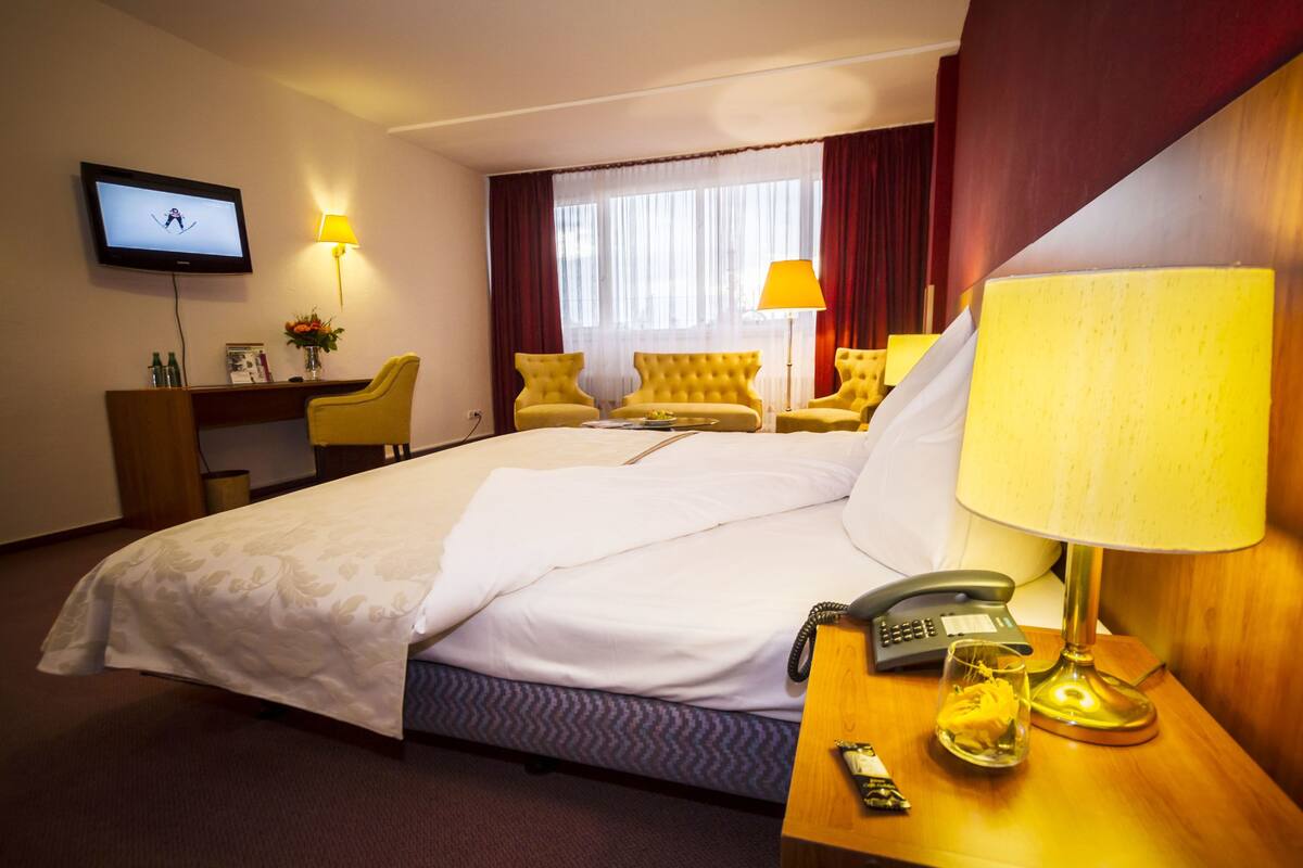 Una habitación de hotel con una cama grande, un escritorio con computadora, un televisor montado en la pared y dos sillones amarillos.