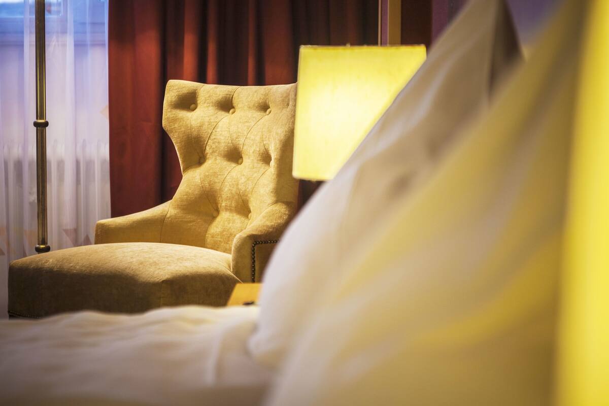 Una habitación de hotel con un sillón capitonado, una mesita de noche y una lámpara.