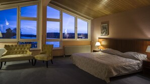 Ein Hotelzimmer mit großem Fenster, einem Bett, einem Sessel und einem Nachttisch mit Lampe.
