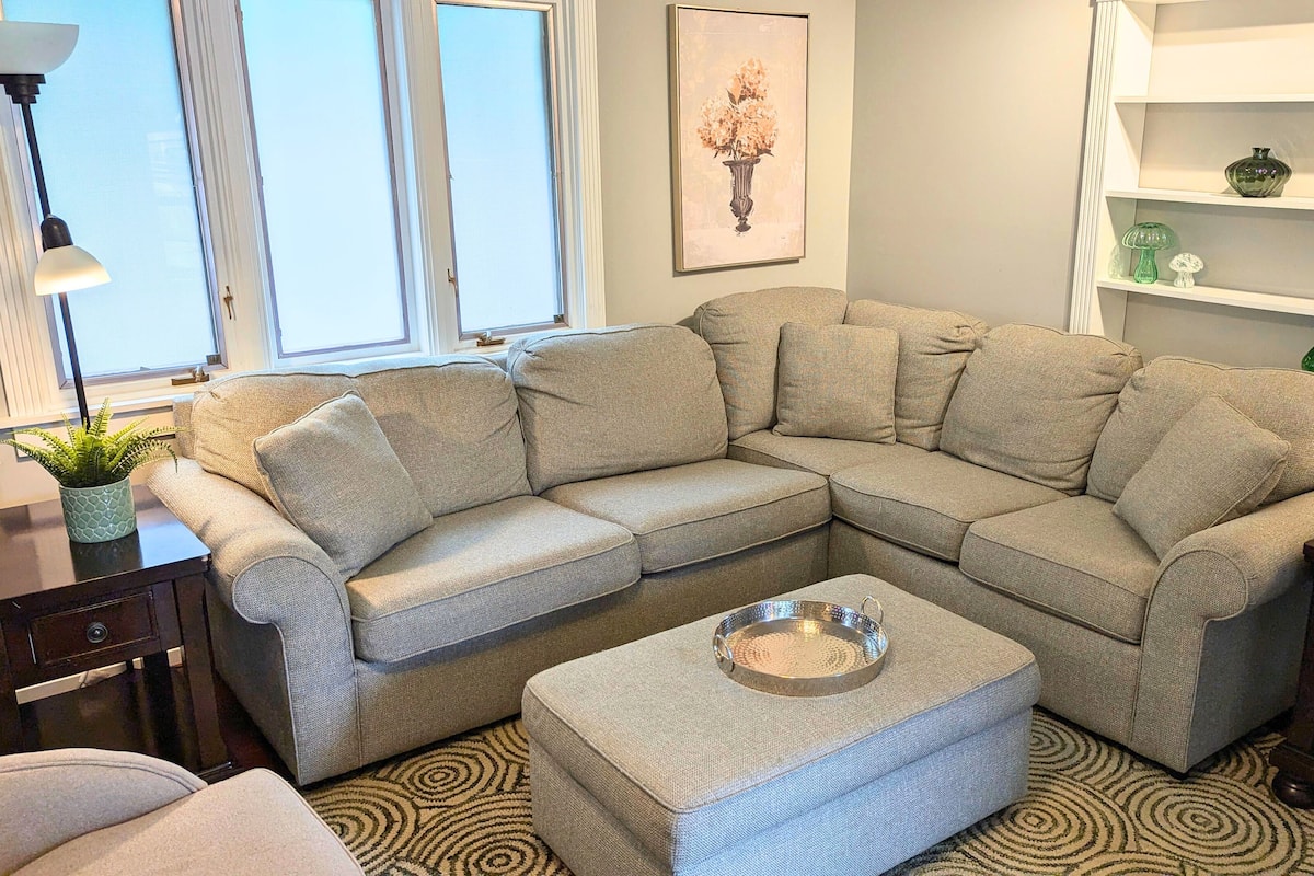 A living room with a sectional sofa, a small side table, a lamp, and a framed picture on the wall.